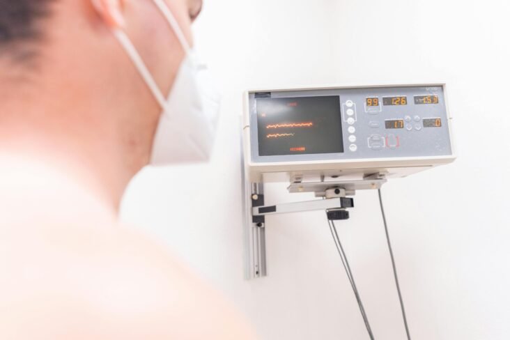 A masked patient in a clinic being monitored by an electronic device.